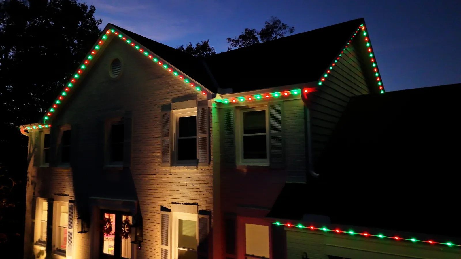 Permanent roofline lighting installed on a two-story home, lit for the holidays