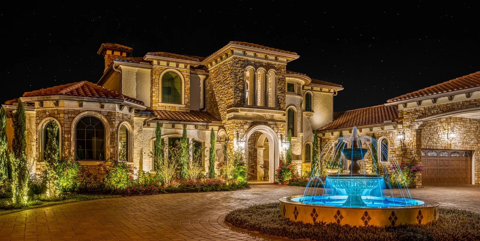 Warm white landscape lighting on a stone home with a lit fountain